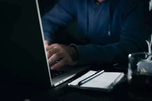 A young hacker working behind a laptop in a dark room — Stock Photo, Image