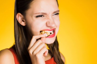 özenle bir sikke ısırmaya çalışıyor sarı bir arka plan üzerinde genç kız