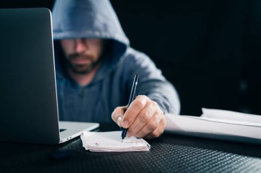 Genç hacker notlar dizüstü oturan bir defter yapma