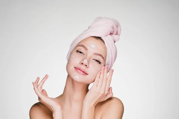 Mignonne jeune fille avec une serviette rose sur la tête en appliquant une crème hydratante blanche sur le visage — Photo