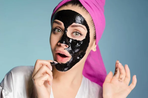 Zaskoczony, młoda dziewczyna z różowy ręcznik na głowie stosuje się oczyszczanie maski na twarz czarny — Zdjęcie stockowe