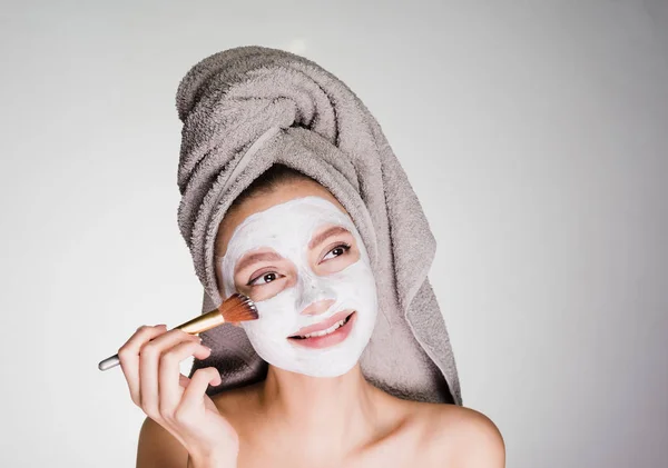 Chica con una toalla en la cabeza se pone en la cara una máscara blanca —  Fotos de Stock
