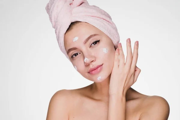 Jeune fille attrayante avec une serviette rose sur sa tête applique une crème hydratante blanche sur le visage — Photo