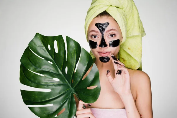 Ένα χαριτωμένο νεαρή κοπέλα με μια πράσινη πετσέτα στο κεφάλι της, βάλτε μια μαύρη μάσκα για τις προβληματικές περιοχές στο πρόσωπό της — Φωτογραφία Αρχείου
