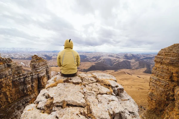 A male traveler sits on the edge of a cliff, enjoys the mountain nature,relaxes and meditates — Stock Photo, Image