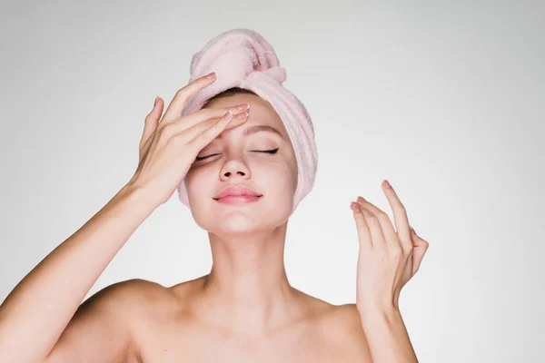 Menina bonito com uma toalha rosa na cabeça, aplicando um creme nutritivo em seu rosto — Fotografia de Stock