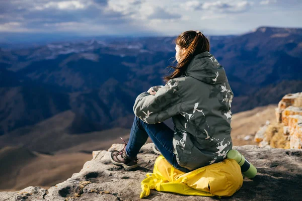 Uma jovem garota ativa senta-se na beira do penhasco, apreciando o ar da montanha e da natureza — Fotografia de Stock