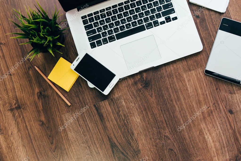 on the wooden floor is a laptop for work, a graphic tablet, a notebook, a smartphone and a potted plant
