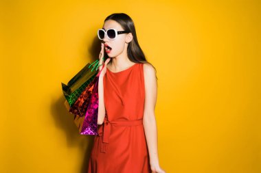 elinde alışveriş ile sarı bir arka plan üzerinde şok genç kız