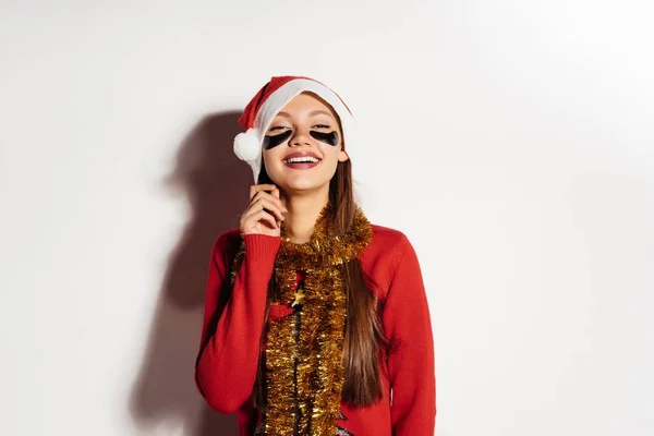 Das überraschte Mädchen im Neujahrsanzug hat unter den Augen eine Hydrogelmaske aufgesetzt — Stockfoto
