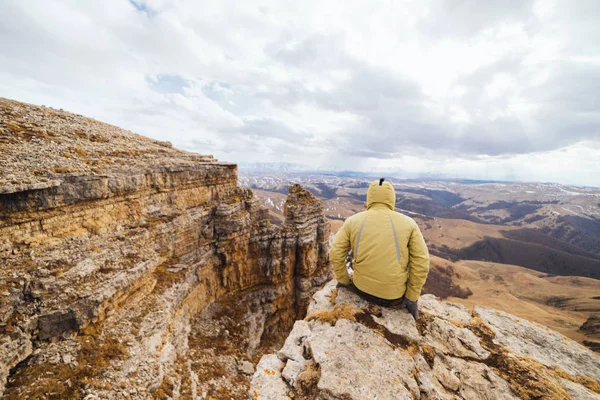 A fickó turisztikai egy dzseki, egy kapucnis, ül a háttérben, a hegyek — Stock Fotó
