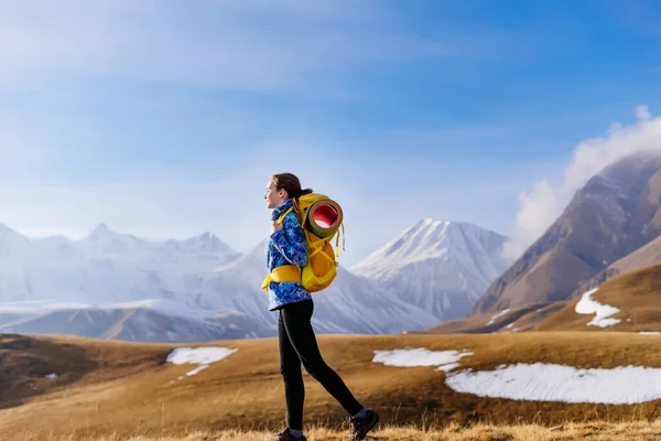 Joven activa en una chaqueta azul viaja a lo largo de la cresta del Cáucaso con una mochila, disfruta de la naturaleza —  Fotos de Stock