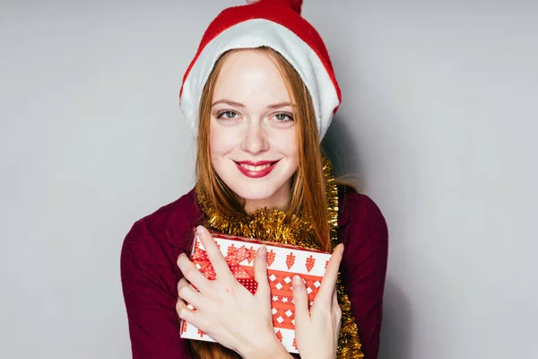 Γέλιο κοκκινομάλλα κοπέλα σε ένα κόκκινο σκουφάκι γιορτάζει το νέο έτος 2018, έλαβε ένα δώρο Χριστουγέννων — Φωτογραφία Αρχείου