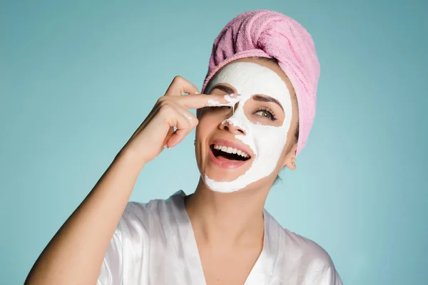 Menina feliz com toalha rosa na cabeça aplicando máscara hidratante branco no rosto — Fotografia de Stock