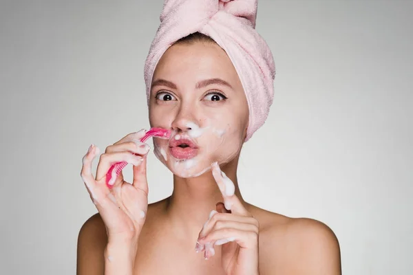 Забавная молодая девушка с розовым полотенцем на голове бреет лицо, как мужчина — стоковое фото