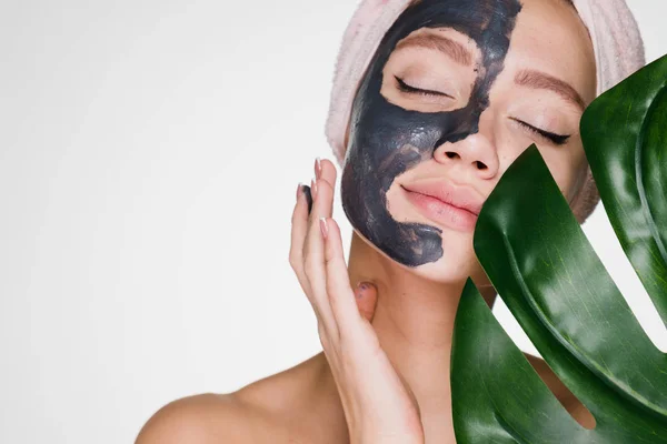 Linda joven disfrutando de tratamientos de spa, media cara máscara de arcilla, sosteniendo una hoja verde — Foto de Stock