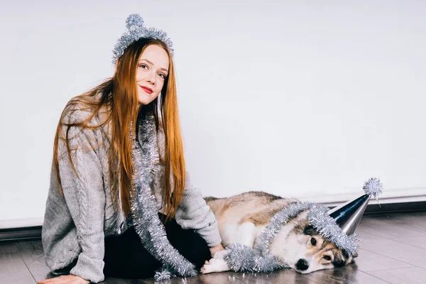 Счастливая симпатичная рыжеволосая девушка, сидящая на полу со своей собакой, в ожидании нового 2018 года и Рождества — стоковое фото