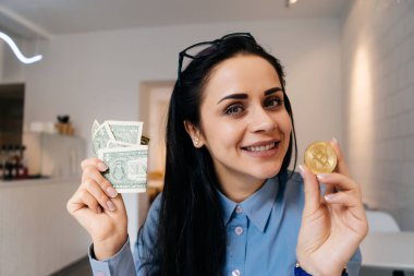 dolar ve altın bitcoin elinde tutan mavi gömlekli başarılı gülümseyen kız