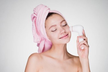 sevimli gülümseyen kız başında pembe havlu ile elektrikli bir fırça kullanarak yüzünde temizlik bir ürpertiyor