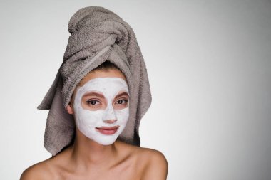 güzel genç kız başında bir havlu ile beyaz bir besleyici maske yüzüne karşı uygulanan.