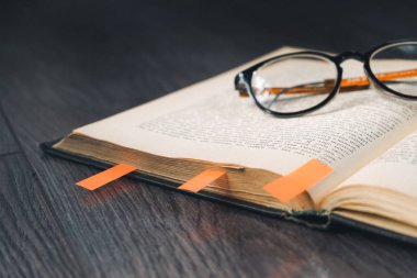 siyah ahşap yüzeyde bir kitap ve gözlük olduğunu