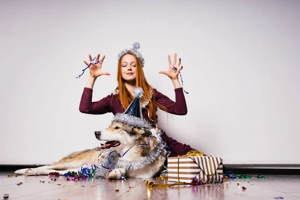 彼女の大きな犬は、新年の雰囲気で床に座っている赤い髪の少女を面白い — ストック写真