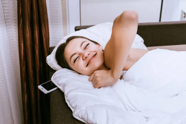 Glücklich schläfriges junges Mädchen liegt frühmorgens im Bett und lächelt — Stockfoto