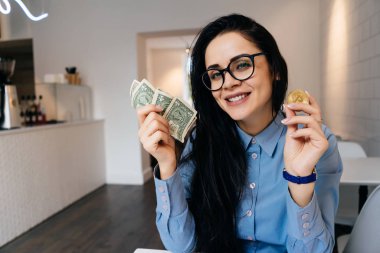 mutlu siyah saçlı kız mavi gömlek ve gözlük dolar ve altın bitcoins onun elinde tutan