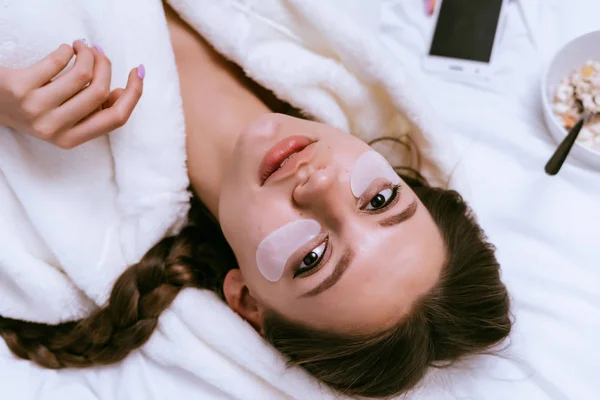 Jovem menina em um manto branco encontra-se em uma cama, sob os olhos manchas brancas — Fotografia de Stock