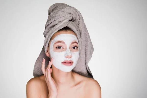Jovem menina atraente com uma toalha na cabeça aplicou uma máscara hidratante branca em seu rosto — Fotografia de Stock