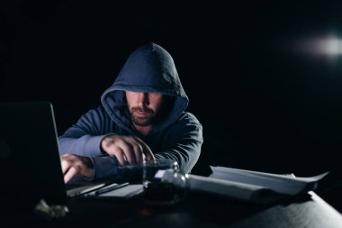adam hacker bir ceket ile bir kukuleta ile bir dizüstü bilgisayar oturuyor