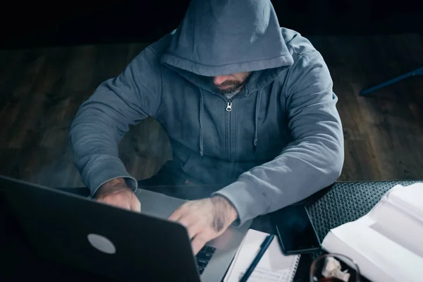 Siedzi facet haker w bluzę z kapturem za laptopa — Zdjęcie stockowe