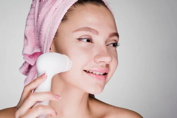Mujer feliz con toalla en la cabeza limpia la piel de la cara con cepillo eléctrico — Foto de Stock