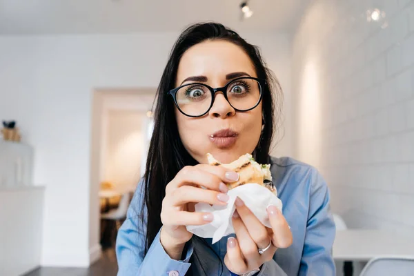 안경에 여자는 사무실에 앉아서 샌드위치를 먹는다 — 스톡 사진