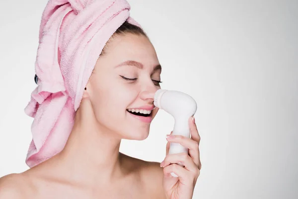 Žena s ručníkem čistí pokožku na tváři s Elektrický kartáč — Stock fotografie