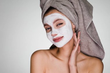 Kafasında havlu olan mutlu bir kadın yüzüne temizleyici bir maske takıyor.