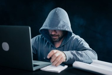 erkek hacker'bir kazak bir kukuleta ile bir dizüstü bilgisayar oturuyor