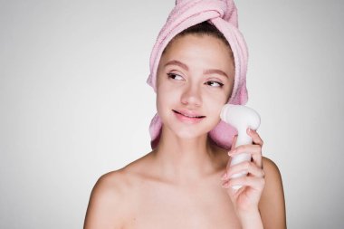 kadının kafasındaki bir havlu ile elektrikli bir fırça ile cildi temizler