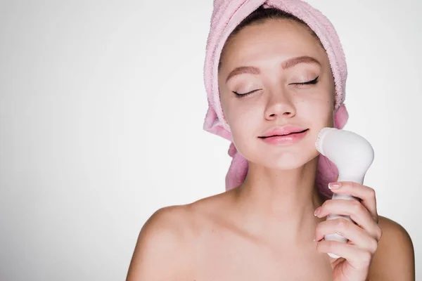 Femme avec une serviette sur la tête nettoie son visage avec une brosse pour un nettoyage en profondeur — Photo