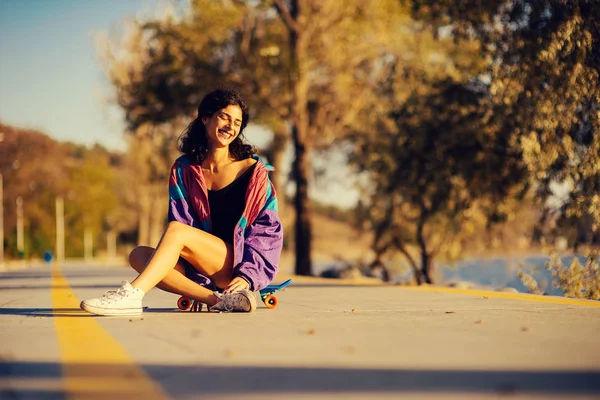 Gelukkig jonge vrouw zit op een skateboard op de achtergrond van het spoor — Stockfoto