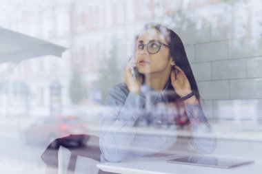 büyük bir pencere bir kadın gözlük masada oturan ve telefonda konuşurken
