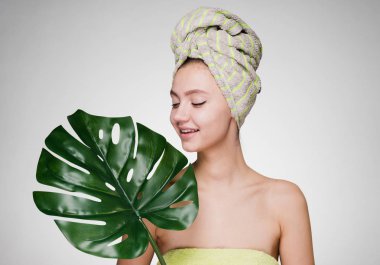 Beyaz bir arka plan üzerinde kadın büyük bir yaprak tutan başında bir havlu ile