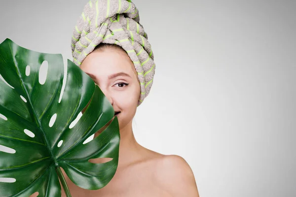 Mujer sobre un fondo blanco con una toalla en la cabeza sosteniendo una hoja grande de una planta — Foto de Stock