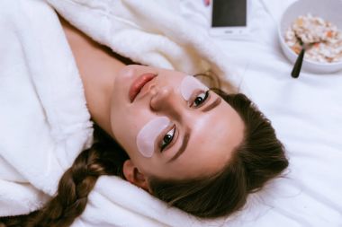 Gözlerinin altındaki yamalar koymak bir yatak üzerinde beyaz bir elbise içinde bir kadın yatıyor