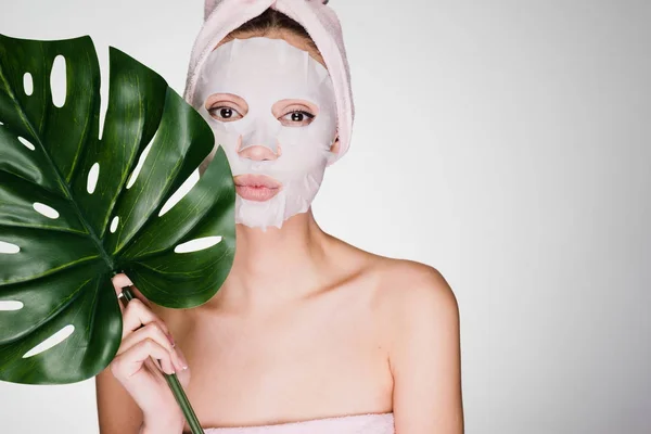 woman with a towel on her head on a gray background apply a cleansing mask on her face