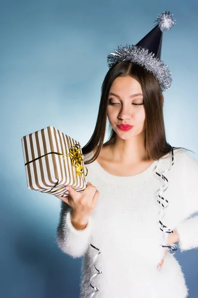 Frau mit Neujahrsmütze hält Geschenk in den Händen und blickt ihn nachdenklich an — Stockfoto