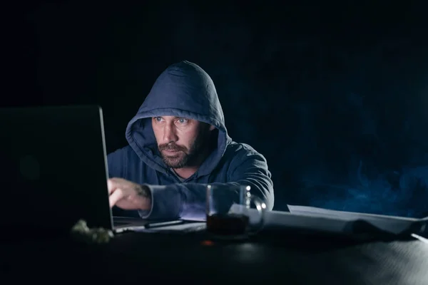 Un homme hacker assis derrière un ordinateur portable et imprime quelque chose — Photo
