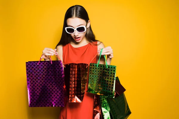 Mädchen in rotem Kleid blickt auf Einkaufstüten auf gelbem Hintergrund — Stockfoto