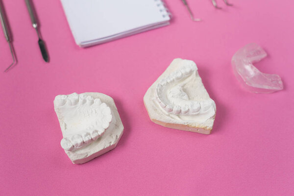 пара слепков зубов рядом с зубными инструментами на розовом столе
