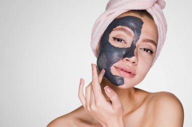 Kafasındaki bir pembe havlu ile güzel bir genç kız bir kil maskesi yüzünün yarısını koydu